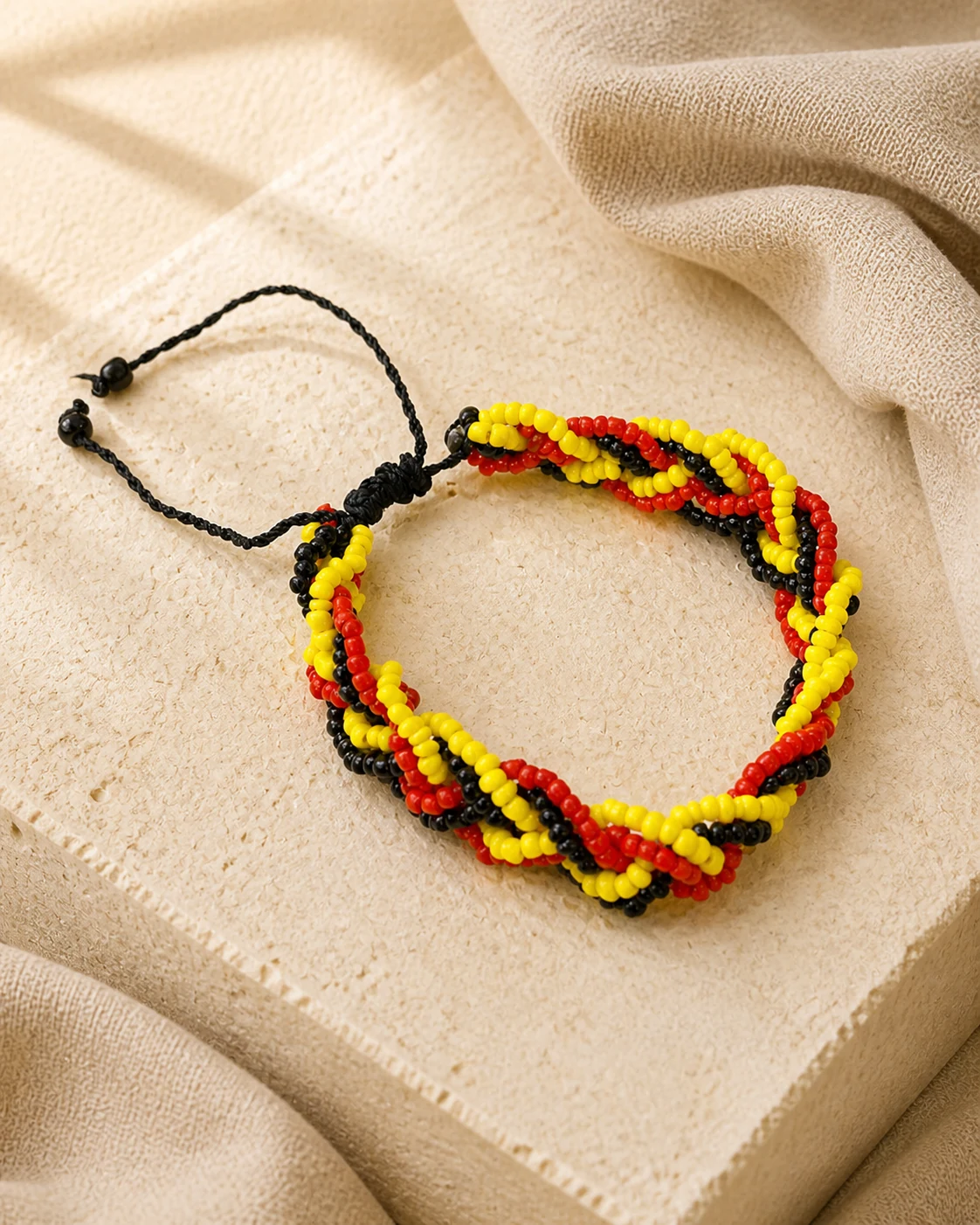 Red, yellow and black braided bead bracelet on warm ivory limestone