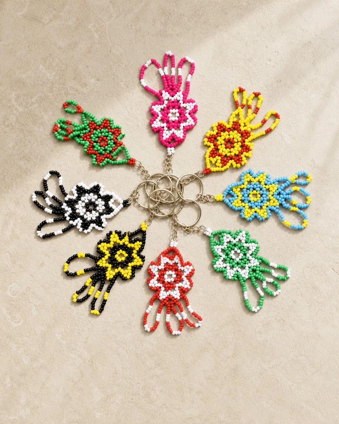 Floral loop beaded keychains arranged in a radial set on warm ivory stone